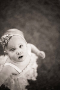 A black and white photograph of a toddler wearing a floral bow in her hair, with striking eyes staring into the camera. Photographed in Burlington Ontario by Mike Streeter.
